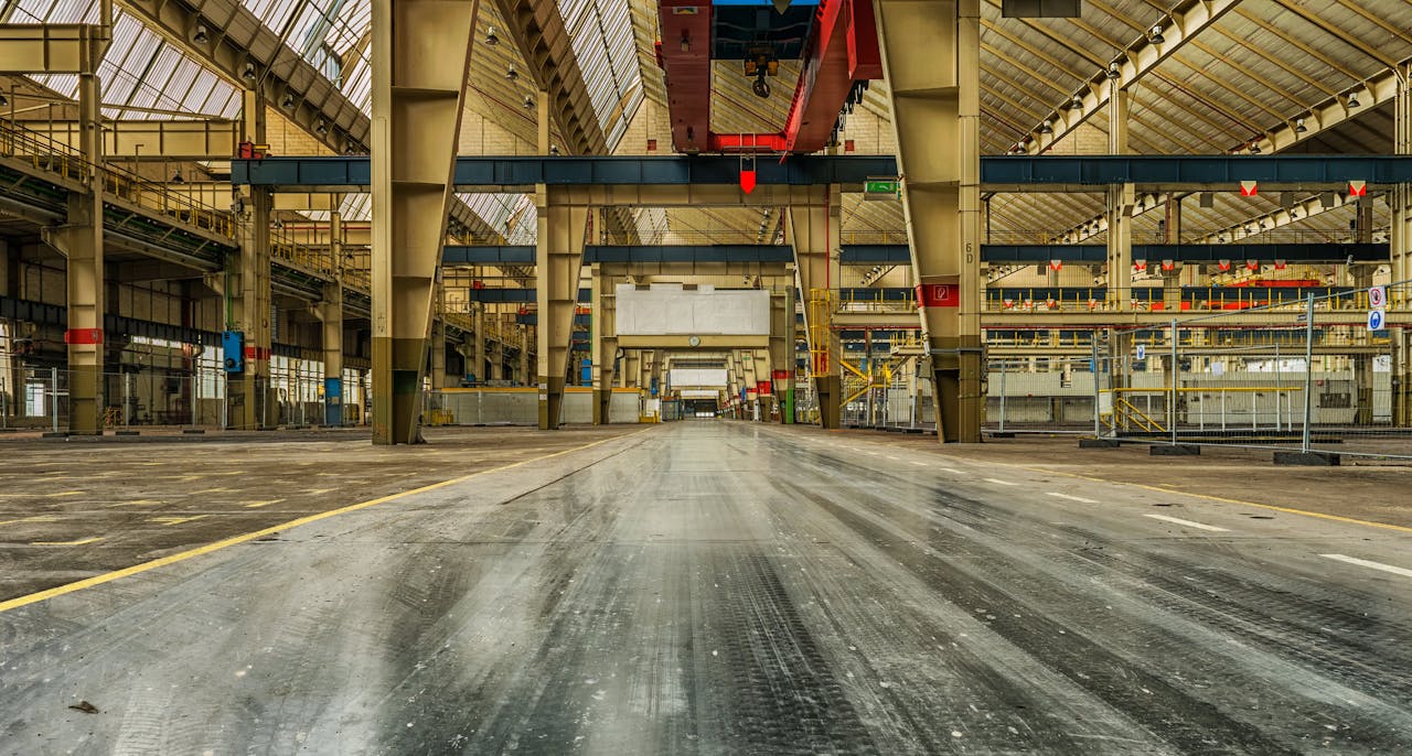 Services Wide view of an empty industrial warehouse with visible cranes and metal structures.