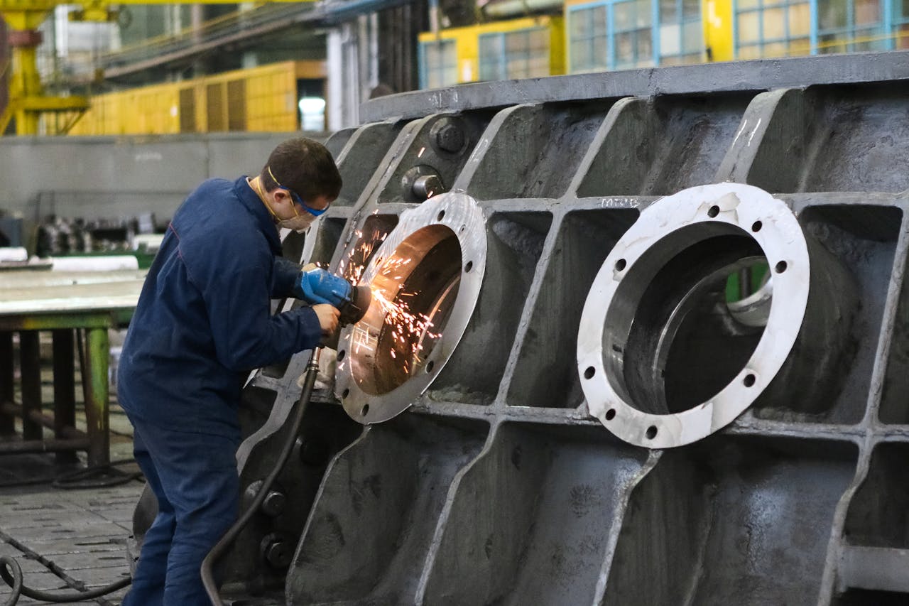 Home A worker in protective gear grinding metal, creating sparks in a factory setting.